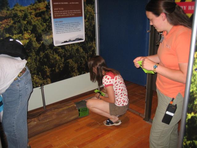 A girl pulls out a box labeled Official Geocache from a log in the exhibit.